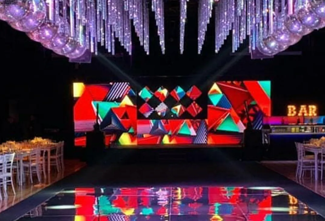 Escenografía LED con rombos y triángulos rojos junto a una pista espejada.