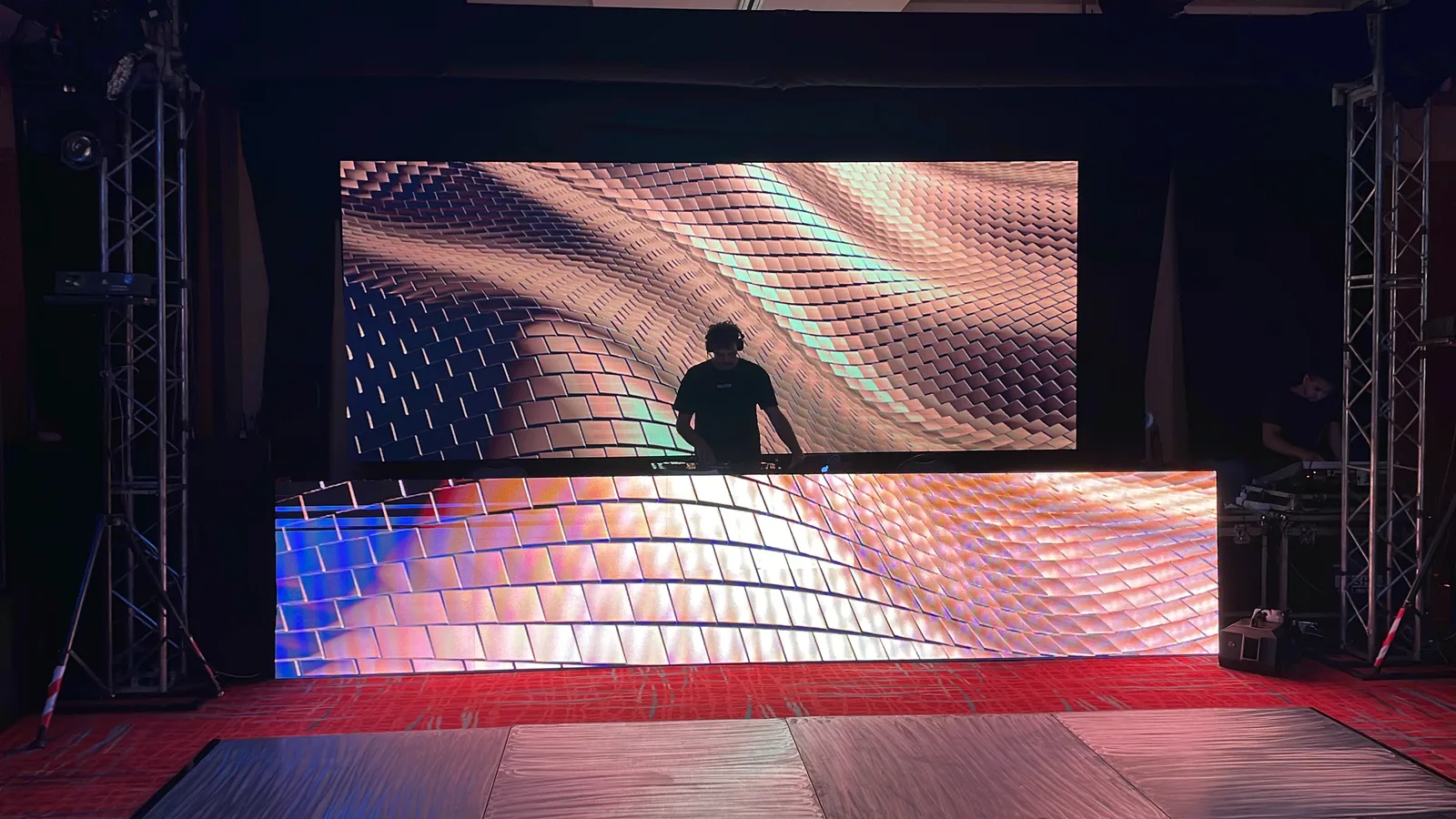 DJ detrás de un frente LED con una segunda pantalla al fondo.