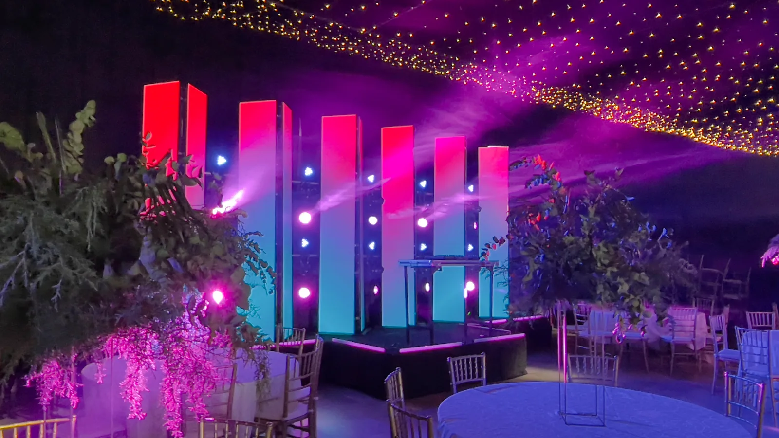 Tótems LED verticales en rojo y azul detrás de una mesa para DJ.