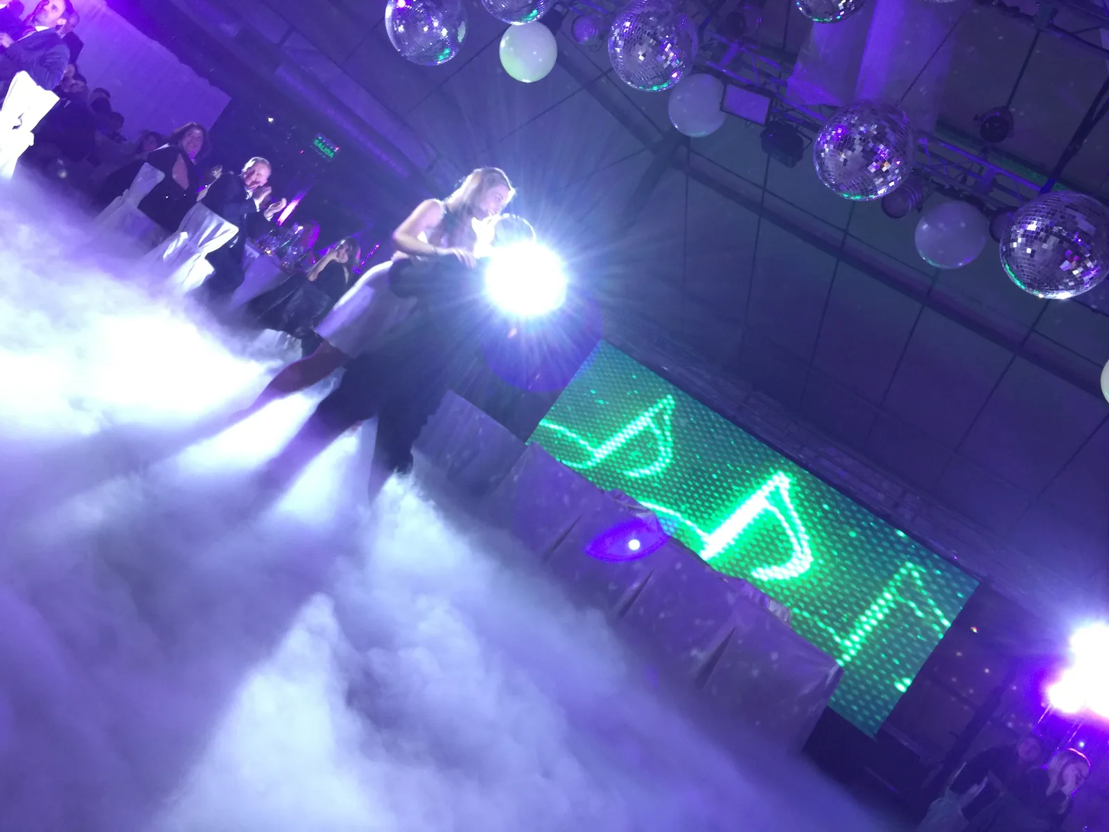 Pareja bailando sobre una nube baja con iluminación violeta.