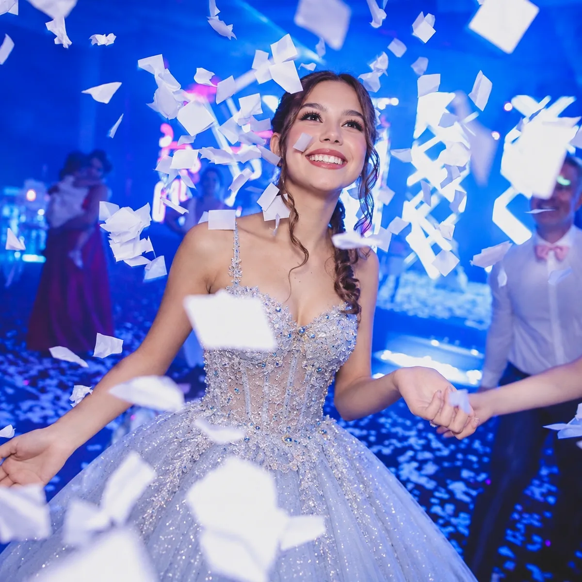 Joven entre papelitos blancos en una fiesta iluminada de azul.