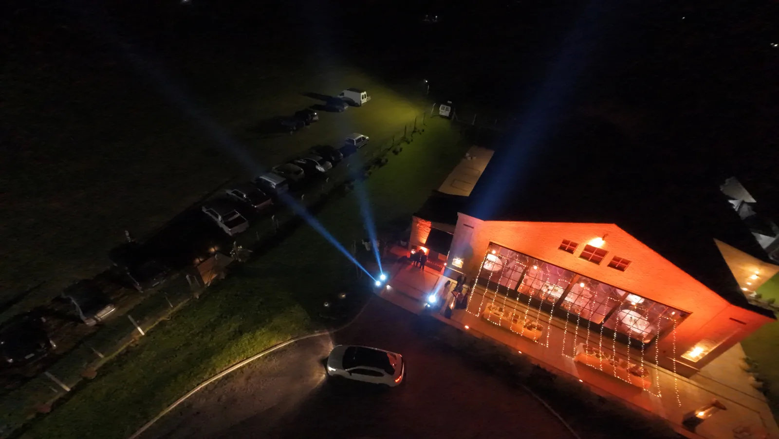 Vista aérea nocturna de un salón con haces de luz hacia el cielo.