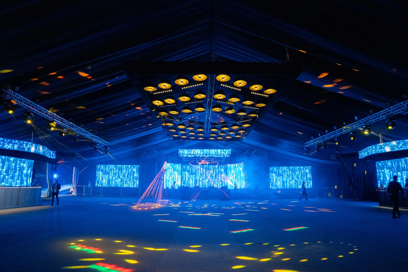 Salón amplio con escenario, pantallas azules y luminarias en el techo.